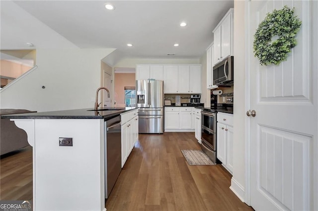 kitchen featuring stainless steel appliances, dark countertops, dark wood finished floors, and a sink