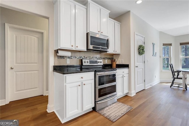 kitchen featuring light wood finished floors, tasteful backsplash, white cabinets, dark countertops, and appliances with stainless steel finishes