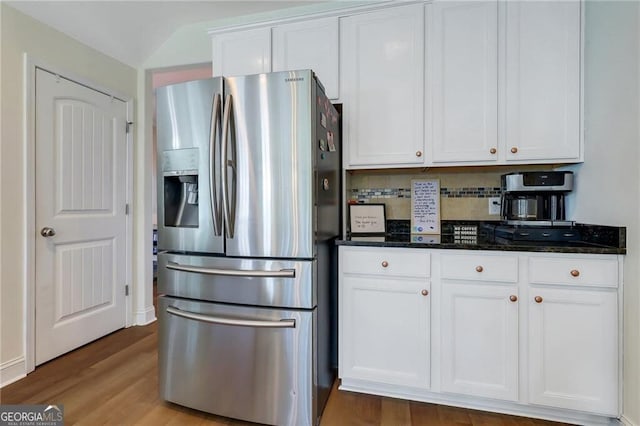 kitchen with stainless steel refrigerator with ice dispenser, tasteful backsplash, white cabinets, dark stone countertops, and wood finished floors