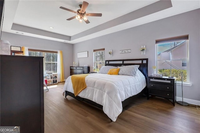 bedroom featuring baseboards, a tray ceiling, wood finished floors, and recessed lighting