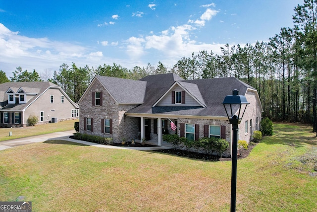 view of front facade with brick siding, a shingled roof, and a front yard