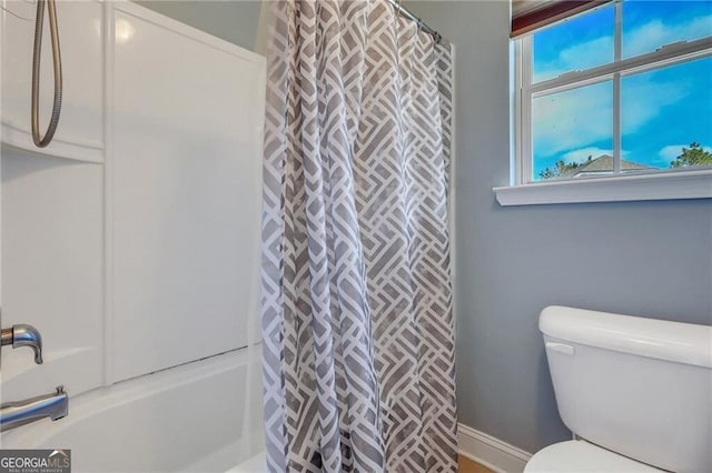 bathroom featuring baseboards, toilet, and shower / bath combo with shower curtain