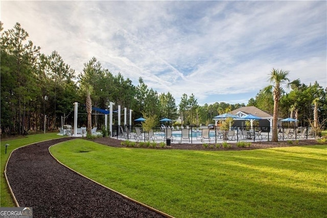 view of community featuring a swimming pool, fence, and a lawn