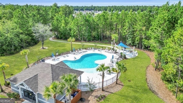 community pool featuring a view of trees, fence, a lawn, and a patio