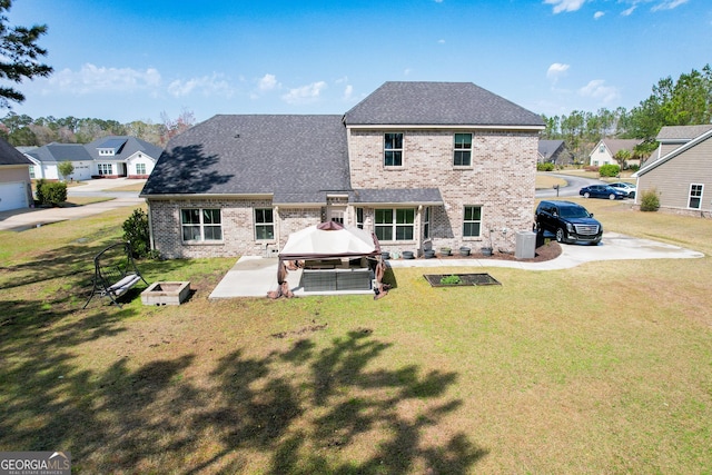 back of property with brick siding, a yard, roof with shingles, a gazebo, and a patio area