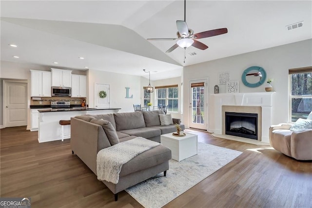 living room featuring dark wood-type flooring, a wealth of natural light, visible vents, and lofted ceiling