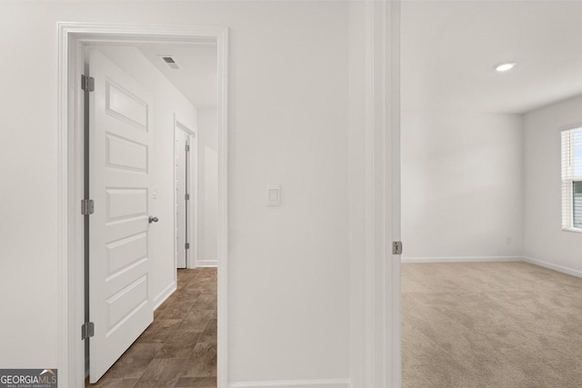 hall with visible vents, baseboards, and dark carpet