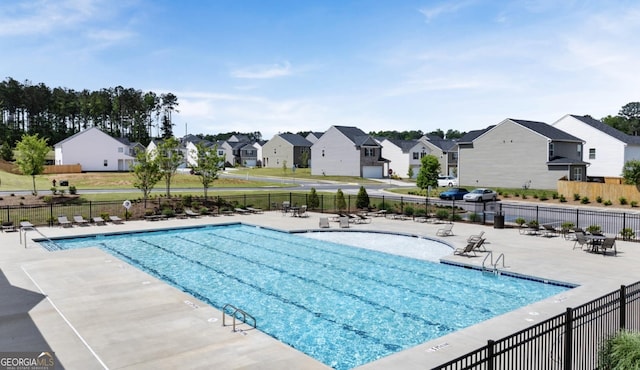 community pool with a patio area, fence, and a residential view