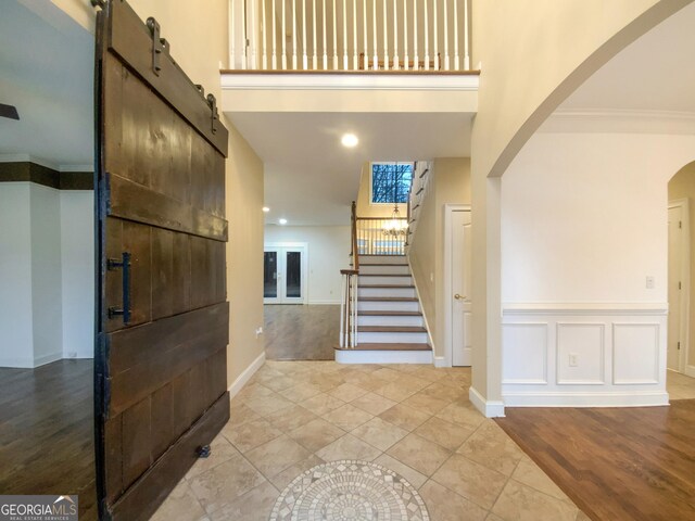 foyer featuring a decorative wall, a high ceiling, ornamental molding, wood finished floors, and stairs