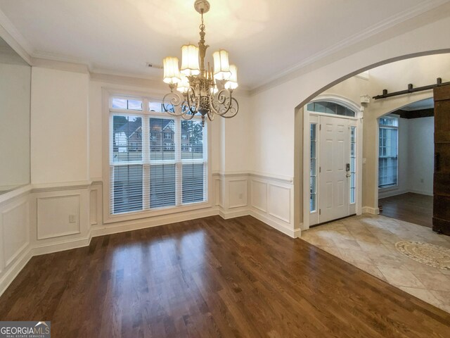 unfurnished dining area with ornamental molding, arched walkways, wood finished floors, and a barn door