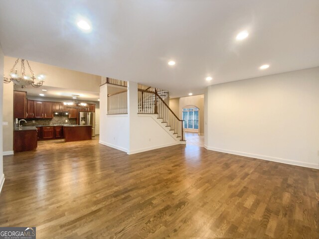 unfurnished living room featuring dark wood-style floors, recessed lighting, stairway, a chandelier, and baseboards