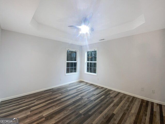 unfurnished room with visible vents, baseboards, a raised ceiling, and dark wood-style flooring