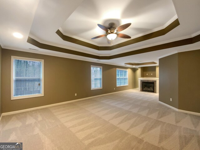 unfurnished living room with ornamental molding, a raised ceiling, light colored carpet, and baseboards