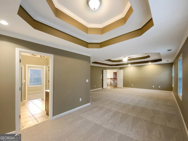 empty room with light carpet, a tray ceiling, baseboards, and crown molding