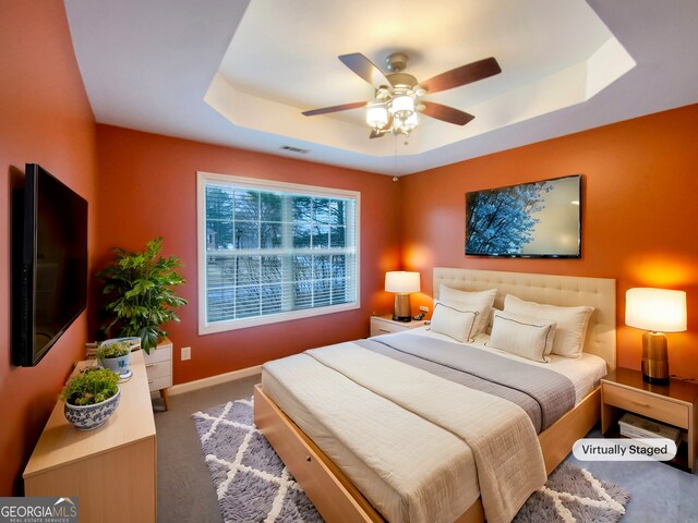 bedroom featuring carpet floors, a tray ceiling, a ceiling fan, and baseboards