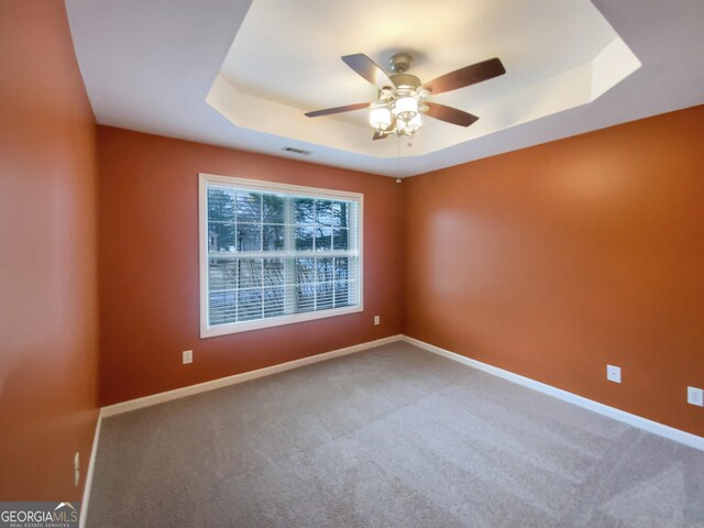 empty room with a raised ceiling, carpet flooring, ceiling fan, and baseboards