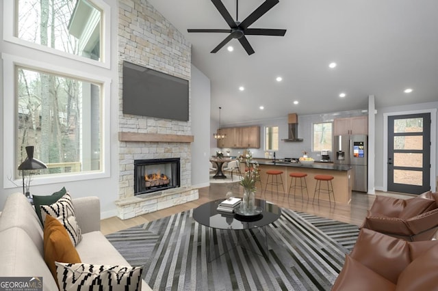 living room featuring baseboards, wood finished floors, a stone fireplace, high vaulted ceiling, and recessed lighting