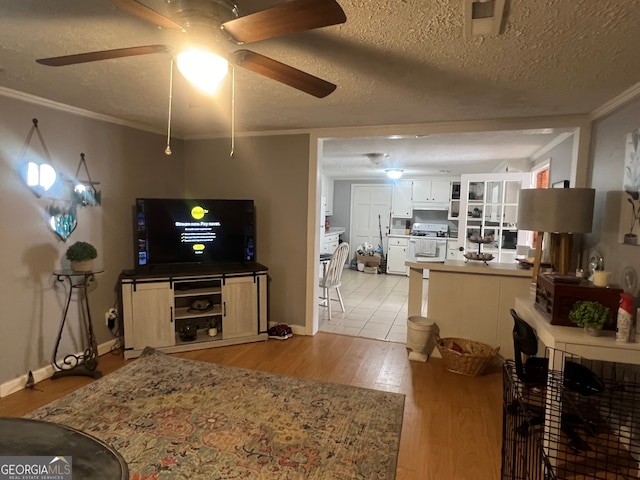 living area with crown molding, light wood-style flooring, a ceiling fan, a textured ceiling, and baseboards