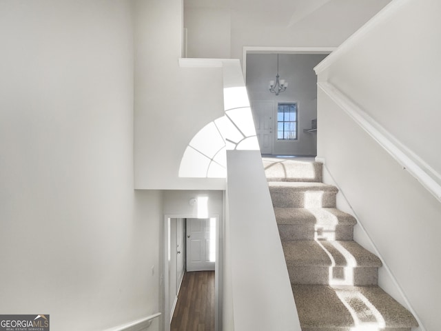 staircase featuring a chandelier, a towering ceiling, baseboards, and wood finished floors