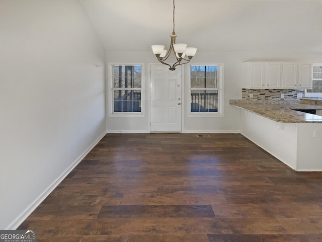 unfurnished dining area with dark wood-style floors, a chandelier, vaulted ceiling, and baseboards