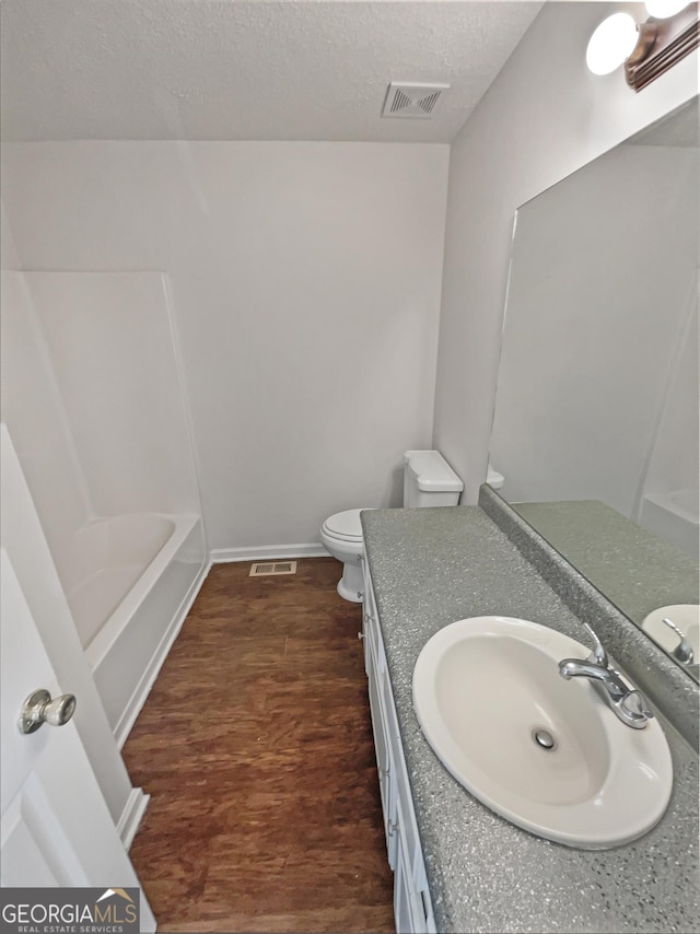 bathroom featuring a textured ceiling, toilet, wood finished floors, vanity, and visible vents