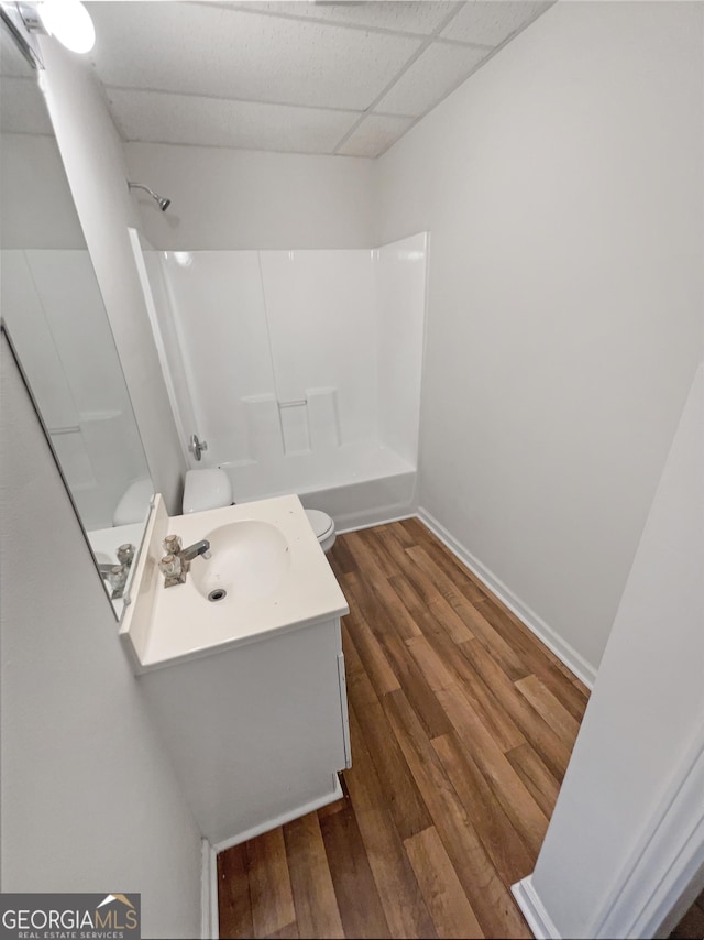 full bath with toilet, a paneled ceiling, wood finished floors, vanity, and shower / washtub combination