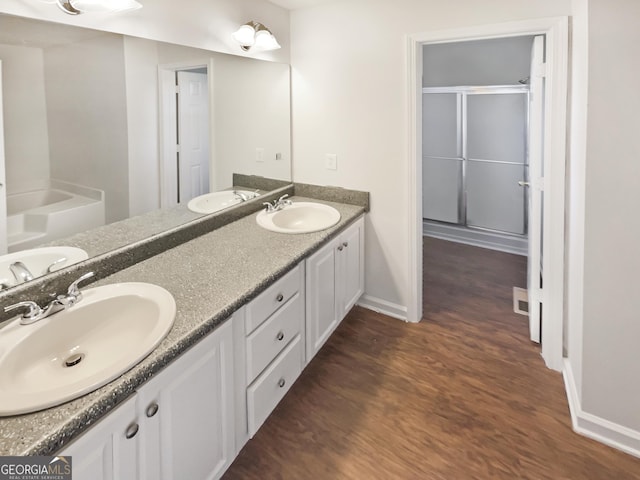 full bathroom featuring double vanity, a shower with door, a sink, and wood finished floors