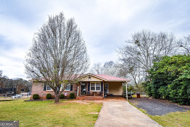 ranch-style home featuring a trampoline, brick siding, metal roof, driveway, and a front lawn