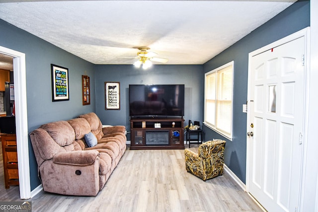 living room featuring a textured ceiling, a fireplace, wood finished floors, a ceiling fan, and baseboards