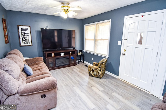 living room with ceiling fan, a textured ceiling, baseboards, and wood finished floors