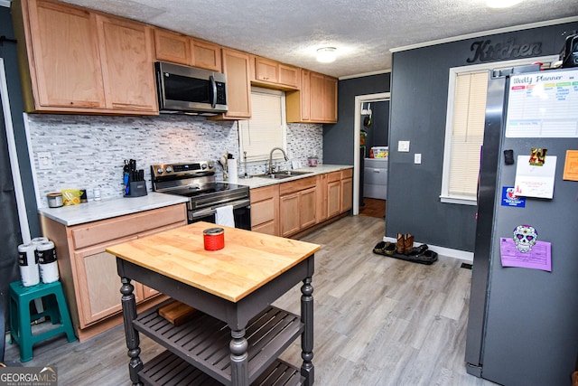 kitchen with light wood finished floors, stainless steel appliances, tasteful backsplash, light countertops, and a sink