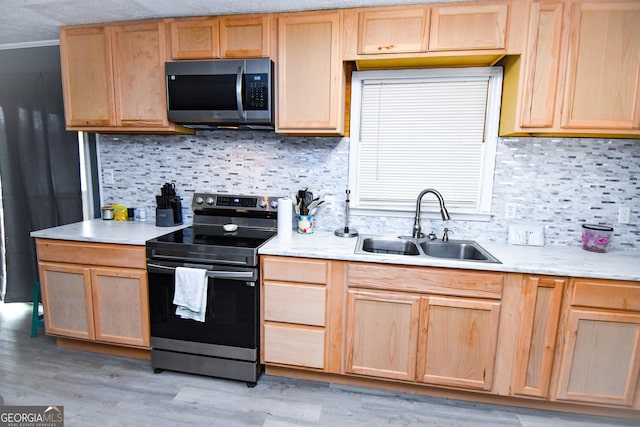 kitchen with light wood-style flooring, stainless steel appliances, light countertops, light brown cabinets, and a sink