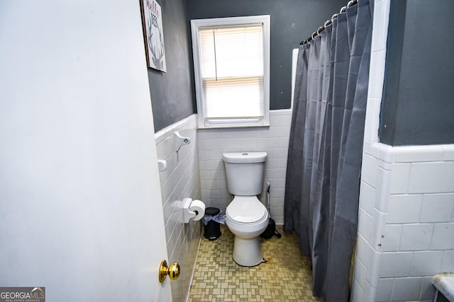 full bath featuring a shower with curtain, wainscoting, toilet, and tile walls