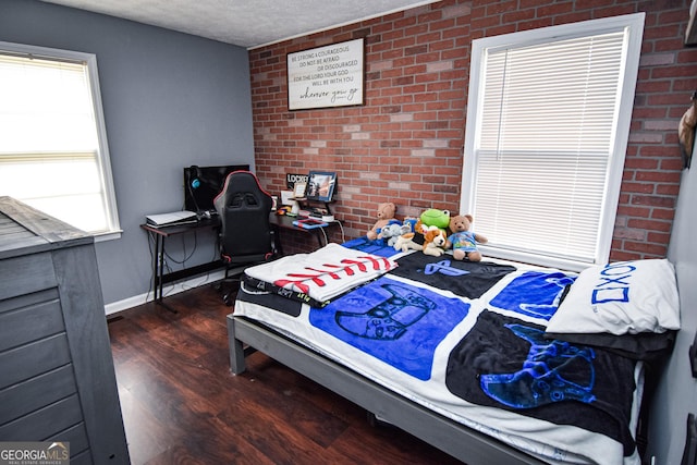 bedroom with brick wall, baseboards, dark wood finished floors, and a textured ceiling