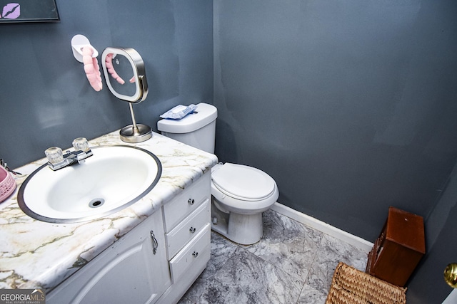 half bathroom with toilet, marble finish floor, vanity, and baseboards