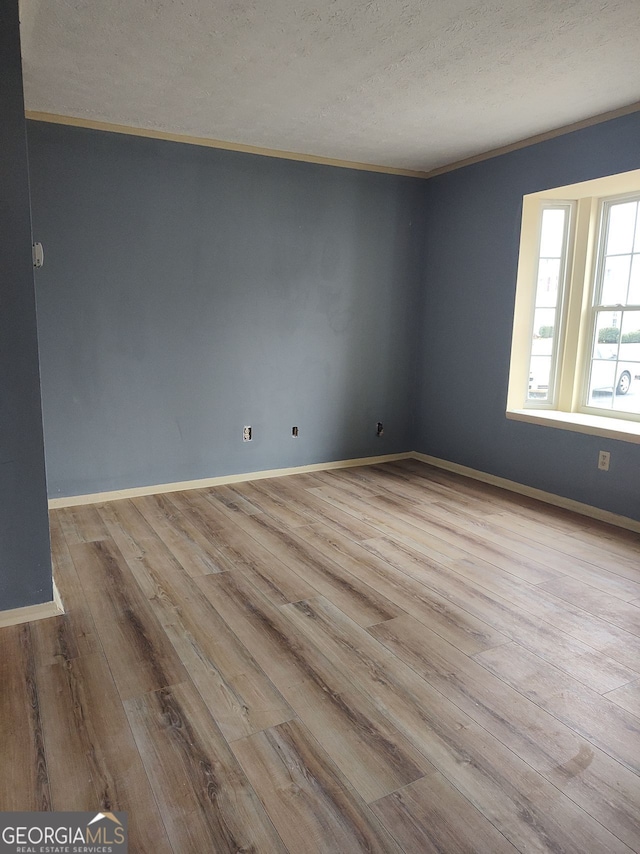 spare room featuring crown molding, a textured ceiling, baseboards, and wood finished floors