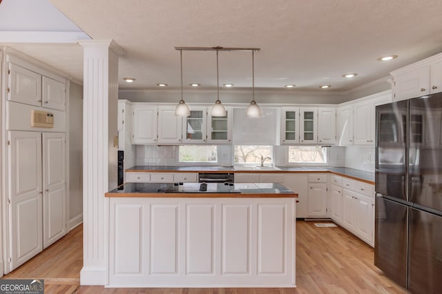 kitchen featuring a peninsula, white cabinetry, freestanding refrigerator, dark countertops, and ornate columns