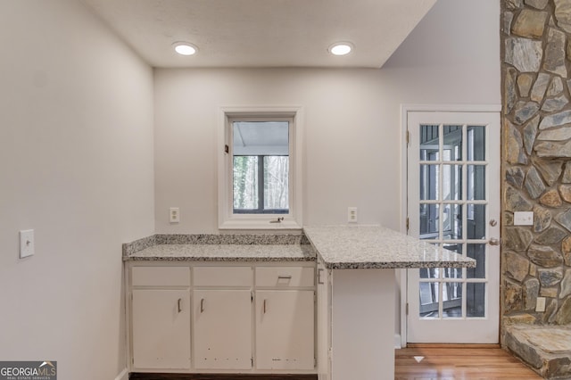 kitchen with a textured ceiling, light wood-style floors, light stone countertops, and white cabinets