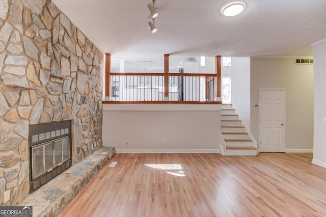 unfurnished living room featuring visible vents, a stone fireplace, baseboards, and wood finished floors