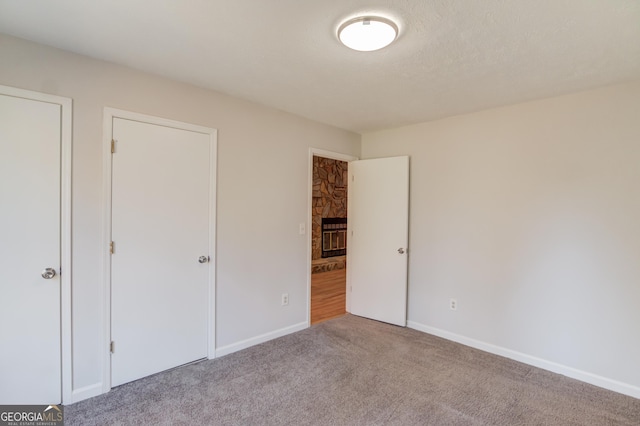 unfurnished bedroom featuring a textured ceiling, carpet, a fireplace, and baseboards