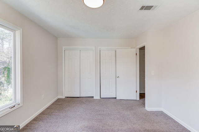 unfurnished bedroom featuring a textured ceiling, visible vents, baseboards, multiple closets, and carpet