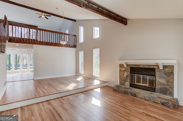 unfurnished living room featuring a stone fireplace, beamed ceiling, wood finished floors, and baseboards