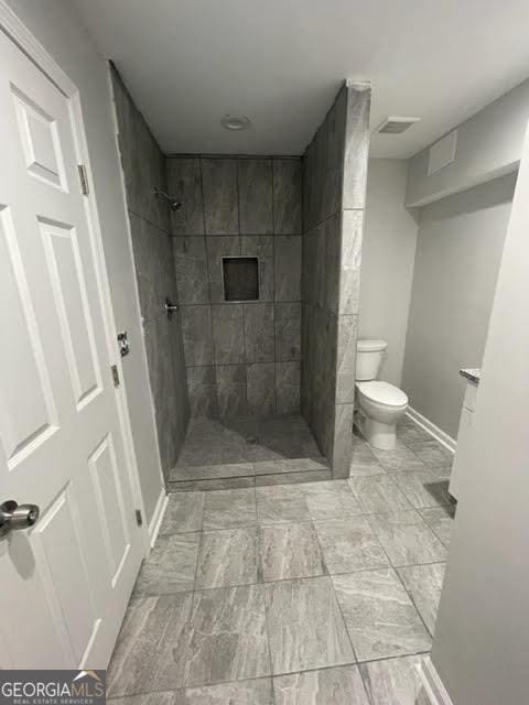 full bath featuring toilet, baseboards, visible vents, and a tile shower