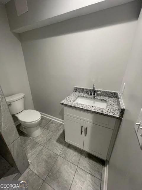 half bathroom with vanity, toilet, and baseboards