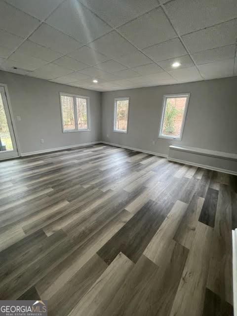 unfurnished room with baseboards, a drop ceiling, and wood finished floors