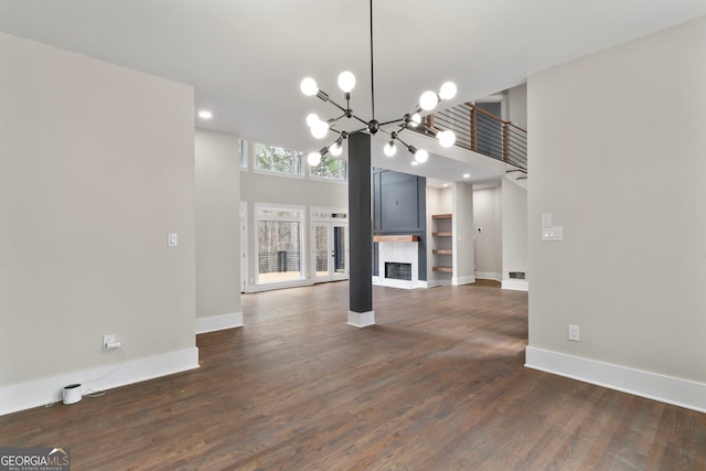 unfurnished living room featuring dark wood-type flooring, a fireplace, baseboards, and an inviting chandelier