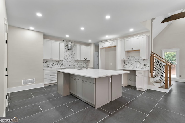 kitchen with dark tile patterned flooring, a center island with sink, visible vents, and white cabinetry