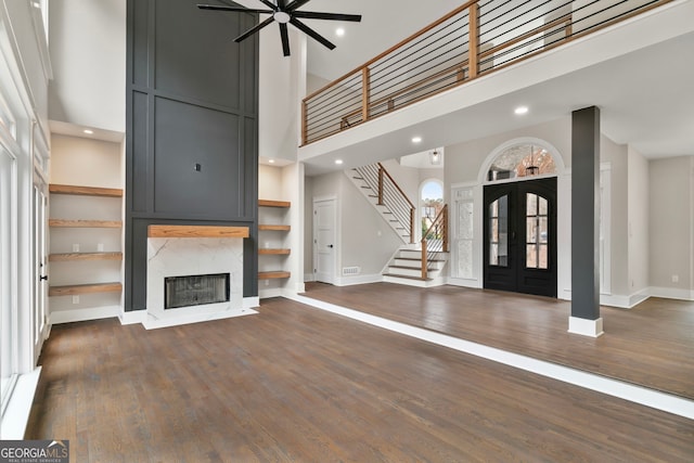 unfurnished living room with dark wood-style floors, stairway, a high ceiling, a high end fireplace, and baseboards