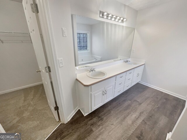 bathroom with double vanity, wood finished floors, a sink, and baseboards