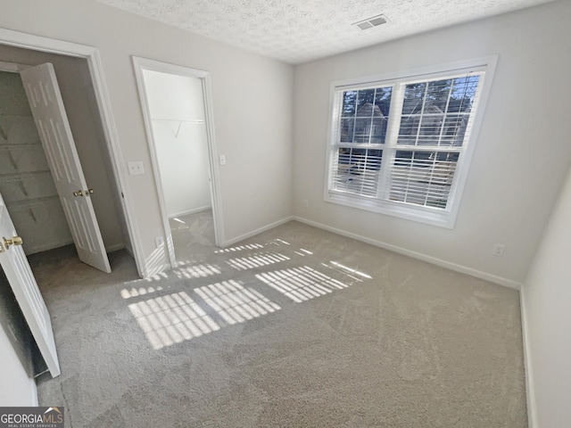 unfurnished bedroom with carpet, visible vents, a spacious closet, a textured ceiling, and baseboards